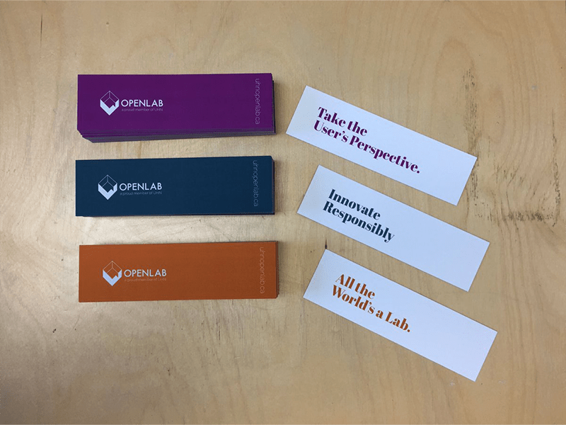 Three piles of rectangular cards of different colours are on a table. They have the OpenLab logo on them. Three cards are placed beside the piles that read "Take the User's Perspective", "Innovate Responsibly" and "All the World's a Lab".