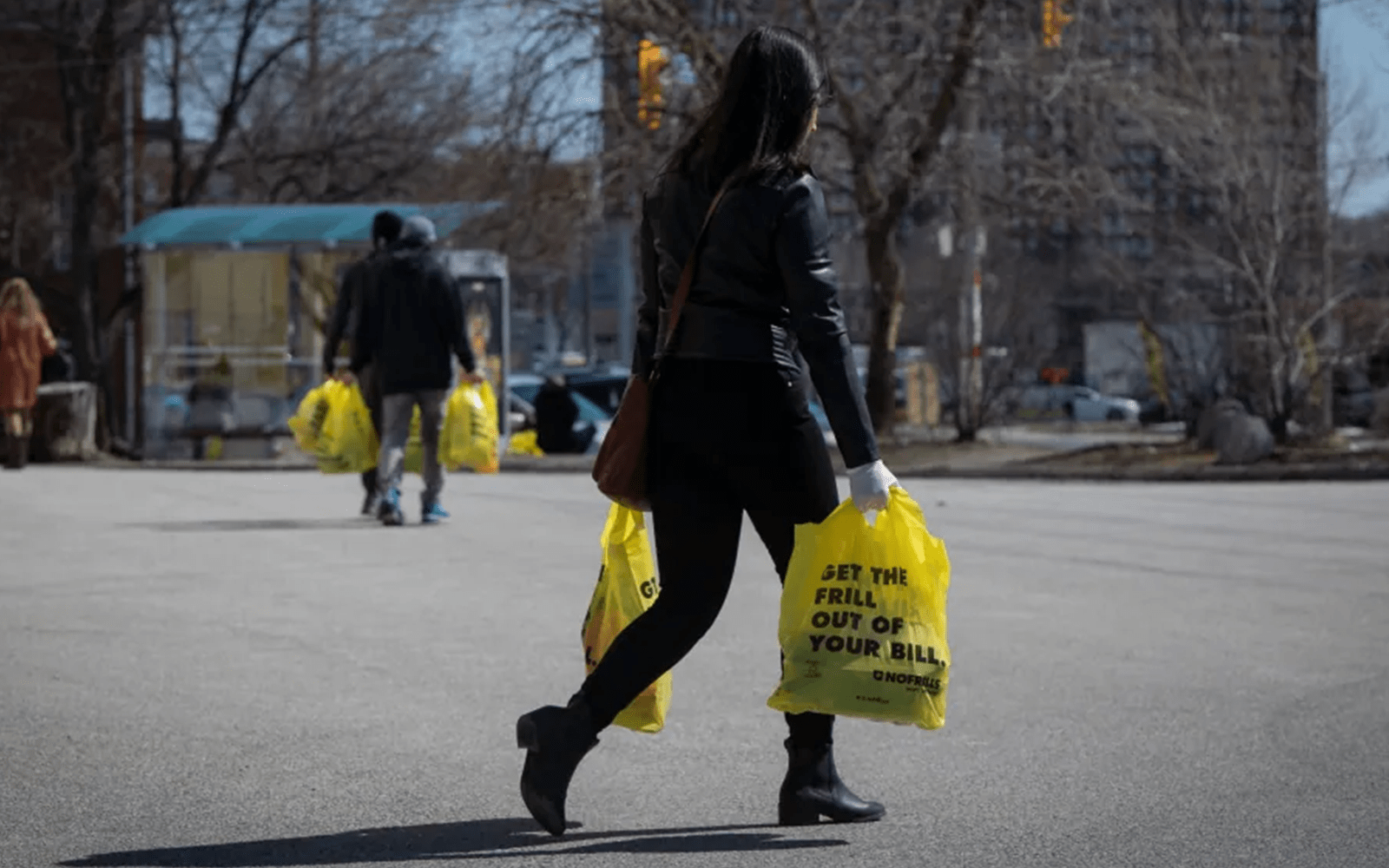 A woman is walking outdoors with two yellow grocery bags.